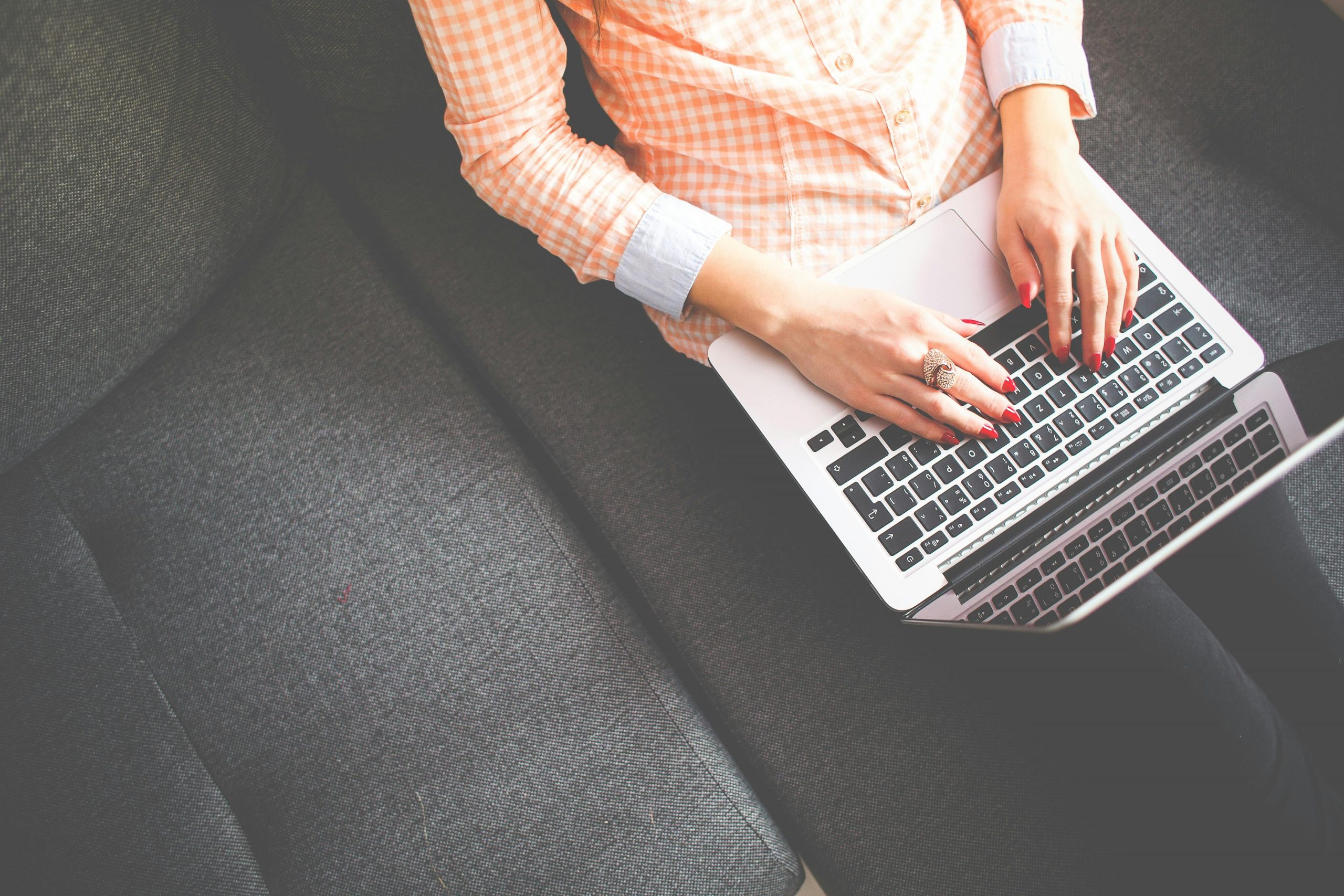 A woman typing on a laptop, sitting on a sofa in casual attire, viewed from above.